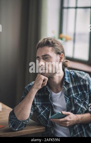 Worried long-haired man holding his smartphone in hands Stock Photo