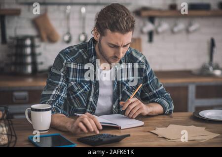 Thoughtful long-haired man writing his ideas into a notebook. Stock Photo