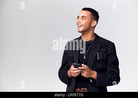 Studio Shot Of Causally Dressed Young Man Using Mobile Phone Looking Off Camera Stock Photo