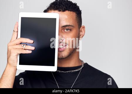 Studio Portrait Of Smiling Young Man Covering Face With Digital Tablet Stock Photo