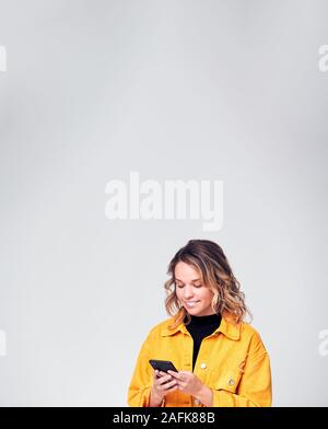 Studio Shot Of Smiling Causally Dressed Young Woman Using Mobile Phone Stock Photo