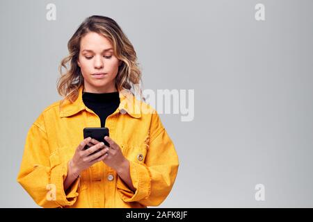 Studio Shot Of Causally Dressed Young Woman Using Mobile Phone Stock Photo