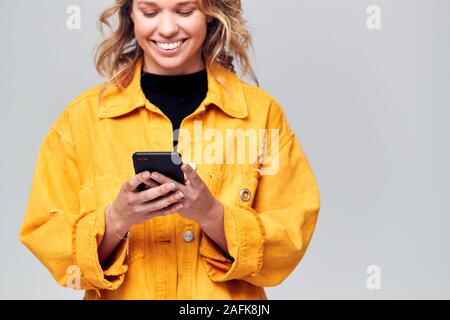 Studio Shot Of Smiling Causally Dressed Young Woman Using Mobile Phone Stock Photo