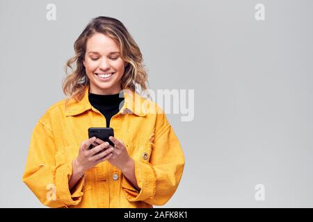 Studio Shot Of Smiling Causally Dressed Young Woman Using Mobile Phone Stock Photo