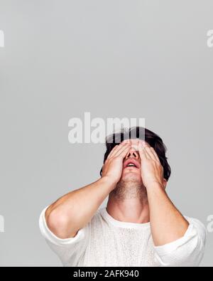 Studio Portrait Of Ashamed Young Man Covering Face With Hands Stock Photo