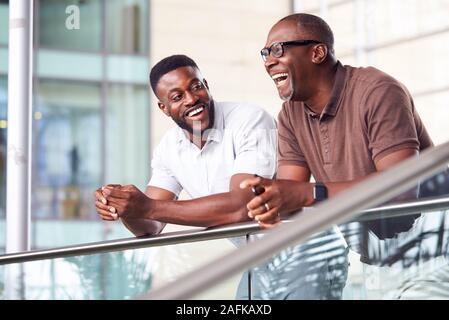 Two Businessmen Having Informal Meeting Standing In Lobby Of Modern Office Stock Photo