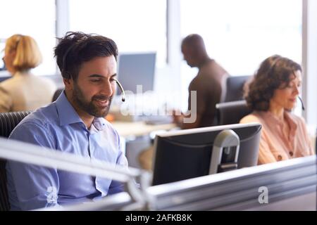 Businessman Wearing Telephone Headset Talking To Caller In Customer Services Department Stock Photo