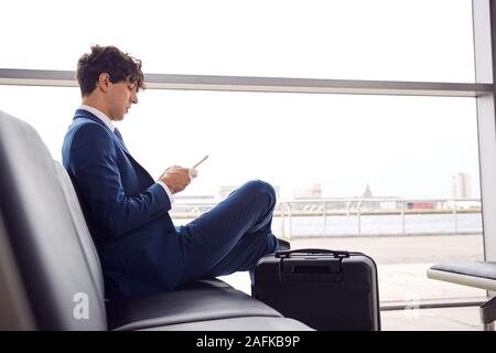 Businessman Sitting In Airport Departure Lounge Using Mobile Phone Stock Photo