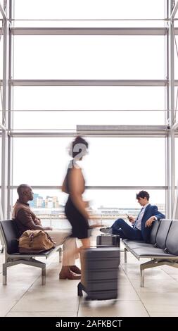 Business Passengers Sitting In Busy Airport Departure Lounge Using Mobile Phones Stock Photo