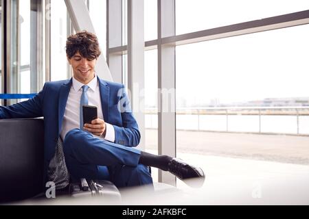 Businessman Sitting In Airport Departure Lounge Using Mobile Phone Stock Photo