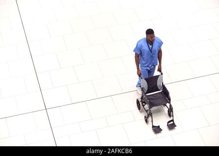 Overhead View Of Male Nurse Pushing Empty Wheelchair Through Lobby Of Modern Hospital Building Stock Photo