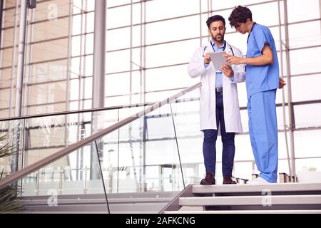 Two Male Doctors Having Informal Meeting In Modern Hospital Looking At Digital Tablet Stock Photo