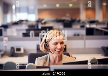 Mature Businesswoman Wearing Telephone Headset Talking To Caller In Customer Services Department Stock Photo