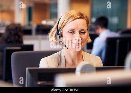 Mature Businesswoman Wearing Telephone Headset Talking To Caller In Customer Services Department Stock Photo