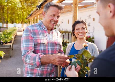 Mature Couple Buying Plants From Male Sales Assistant In Garden Center Stock Photo