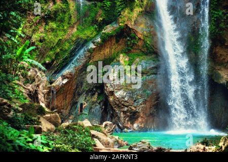 Happy woman traveler with raised arms enjoying life at a beautiful rainforest waterfall in Bali Stock Photo