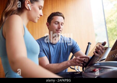 Woman In Gym With Personal Trainer Analysing Performance Using Smart Watch And Digital Tablet Stock Photo