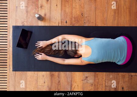 Overhead View Of Woman Stretching On Exercise Mat Using Digital Tablet Stock Photo