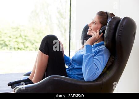 Woman Relaxing In Chair At Home Listening To Music Or Podcast Music On Wireless Earphones Stock Photo