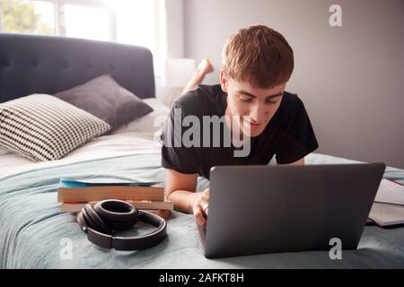 Male College Student Lies On Bed In Shared House Working On Laptop Stock Photo