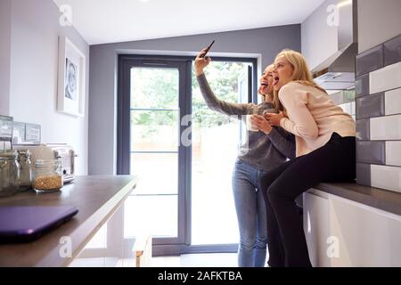 Two Female College Students Taking Selfie In Rented House Kitchen Stock Photo