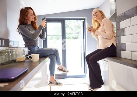 Two Female College Students Taking Selfie In Rented House Kitchen Stock Photo