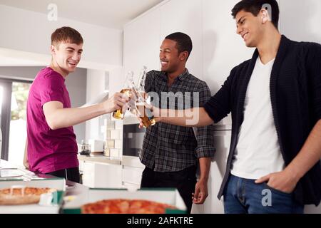 Group Of Male College Students In Shared House Kitchen Drinking Beer And Eating Pizza Together Stock Photo