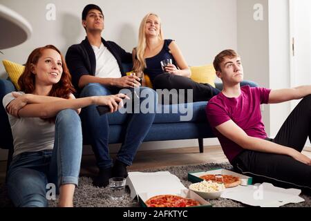 Group Of College Students In Shared House Watching TV And Eating Pizza Stock Photo