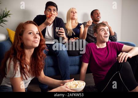 Group Of College Students In Shared House Watching TV And Eating Popcorn Stock Photo