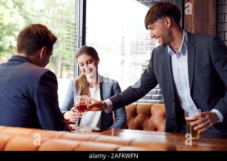 Businessman Buying Round Of Drinks For Colleagues Meeting And Socializing In Bar After Work Stock Photo