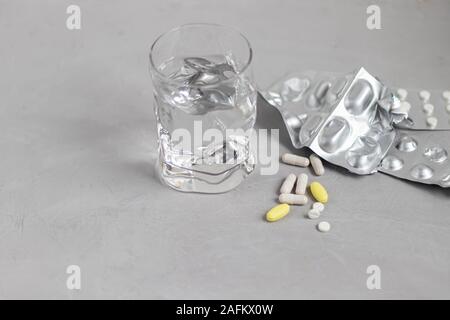 Pills on a gray background. Near a glass of water. Records with medicines. Stock Photo