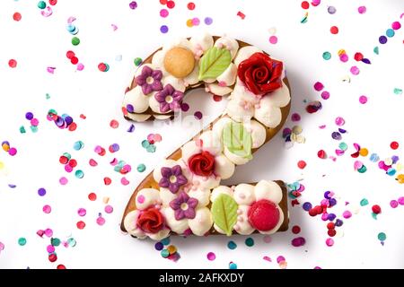 Number two cake decorated with flowers, macarons and confetti isolated on white background. Copy space Stock Photo