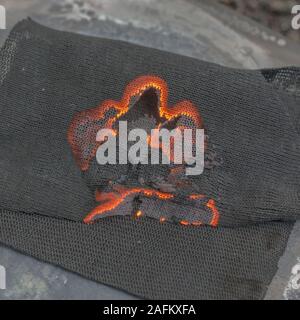 Survival skills. Close shot of burning charcloth. Material is used in fire making, & made by pyrolysis of vegetable fibre: linen, cotton or jute. Stock Photo