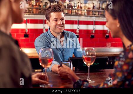Woman Paying Barman For Drinks At Bar After Work Using Contactless Card Stock Photo