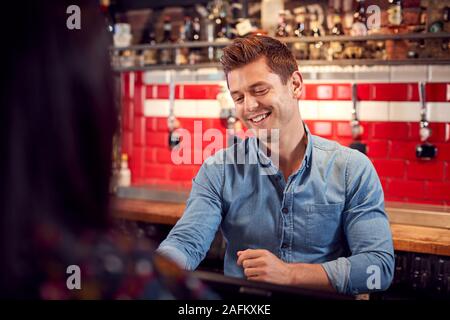 Male Bar Tender Standing Behind Counter Serving Drinks To Customer Stock Photo