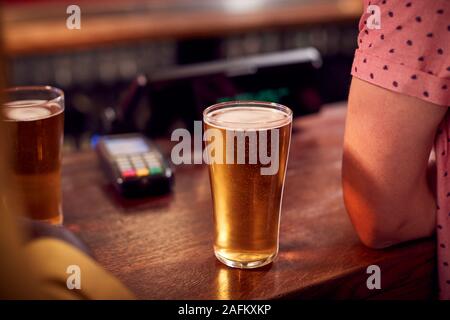 Close Up Of Pints Of Beer Standing On Counter Of Bar With Customer Stock Photo