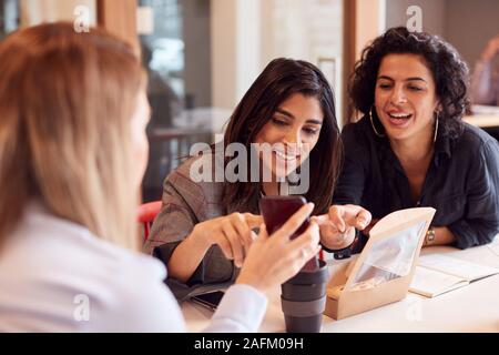 Group Of Young Businesswomen Sitting Around Table Having Working Lunch And Looking At Mobile Phones Stock Photo