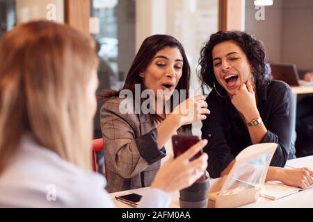 Group Of Young Businesswomen Sitting Around Table Having Working Lunch And Looking At Mobile Phones Stock Photo