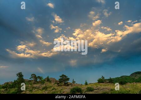 Evening landscape in the mountains. The rays of the setting sun illuminate the clouds. Hill with sparse pine trees. Bayanaul National Park. Kazakhstan Stock Photo