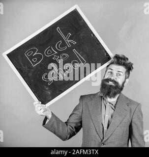 Teacher bearded man holds blackboard with inscription back to school green background. Keep working. Teaching stressful occupation. Teacher with tousled hair stressful about school year beginning. Stock Photo