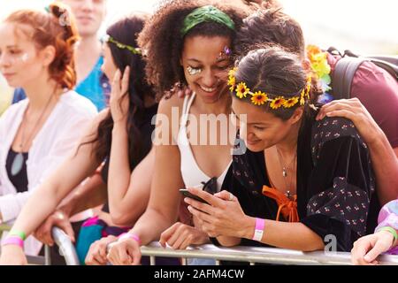 Young Friends In Audience Behind Barrier At Outdoor Music Festival Looking At Mobile Phone Stock Photo