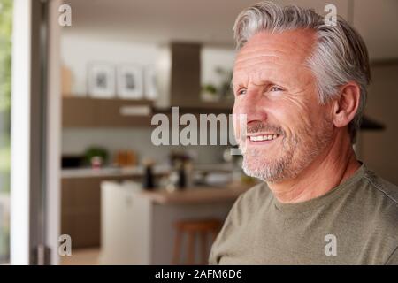 Smiling Senior Man Standing And Looking Out Of Kitchen Door Stock Photo