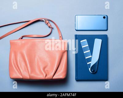 Pink coral female leather bag with accessories in classic blue 2020 color over blue background. Color of year 2020 concept for fashion and clothing industry. Stock Photo