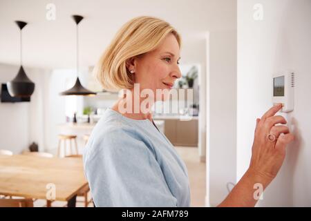 Close Up Of Mature Woman Adjusting Central Heating Temperature At Home On Thermostat Stock Photo