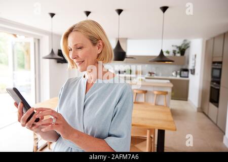 Mature Woman Using App On Mobile Phone To Control Central Heating Temperature In House Stock Photo