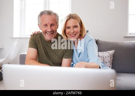 Senior Couple Sitting On Sofa At Home Making Video Call Using Laptop Computer Together Stock Photo