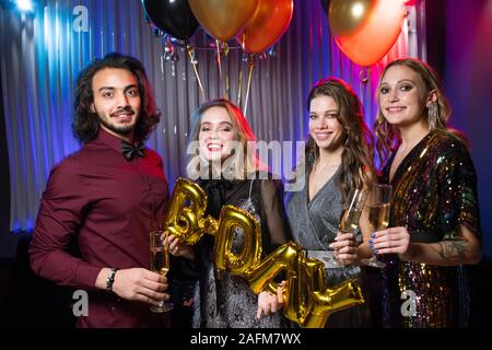 Three happy girls and young man holding flutes of champagne and balloons Stock Photo