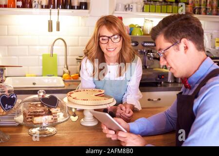 Shot of happy small business owner woman and young waiter standing at counter and using digital tablet while working together. Small business. Stock Photo
