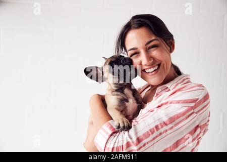 Studio Portrait Of Smiling Young Woman Holding Affectionate Pet French Bulldog Puppy Stock Photo