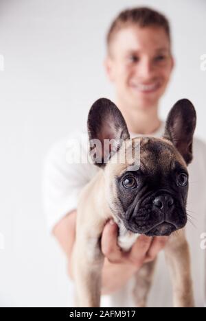 Studio Portrait Of Smiling Young Man Holding Pet French Bulldog Puppy Stock Photo